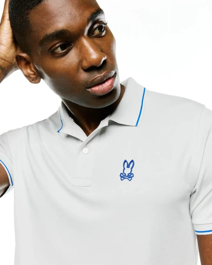 Men's Joji Performance Polo, light grey pique knit with a classic fit, features a two-button placket, blue tipping on the collar and sleeve cuffs, and an embroidered blue Psycho Bunny skull logo on the left chest.