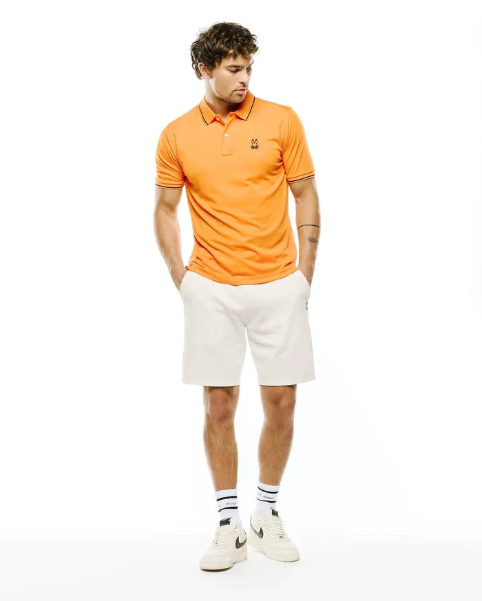 Mens Joji Performance Polo, vibrant orange slim fit pique polo with black trim on collar and cuffs, featuring a small embroidered Psycho Bunny skull logo on the left chest.