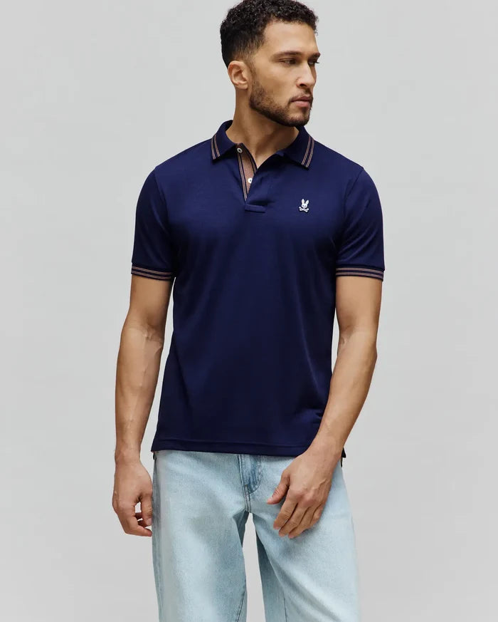 Mens Kenyon Lightweight Pique Polo in navy blue, featuring a classic fit, pique fabric, and a small embroidered white Psycho Bunny skull logo on the left chest. Collar and sleeve cuffs have orange and white stripe accents.