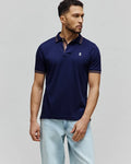 Mens Kenyon Lightweight Pique Polo in navy blue, featuring a classic fit, pique fabric, and a small embroidered white Psycho Bunny skull logo on the left chest. Collar and sleeve cuffs have orange and white stripe accents.