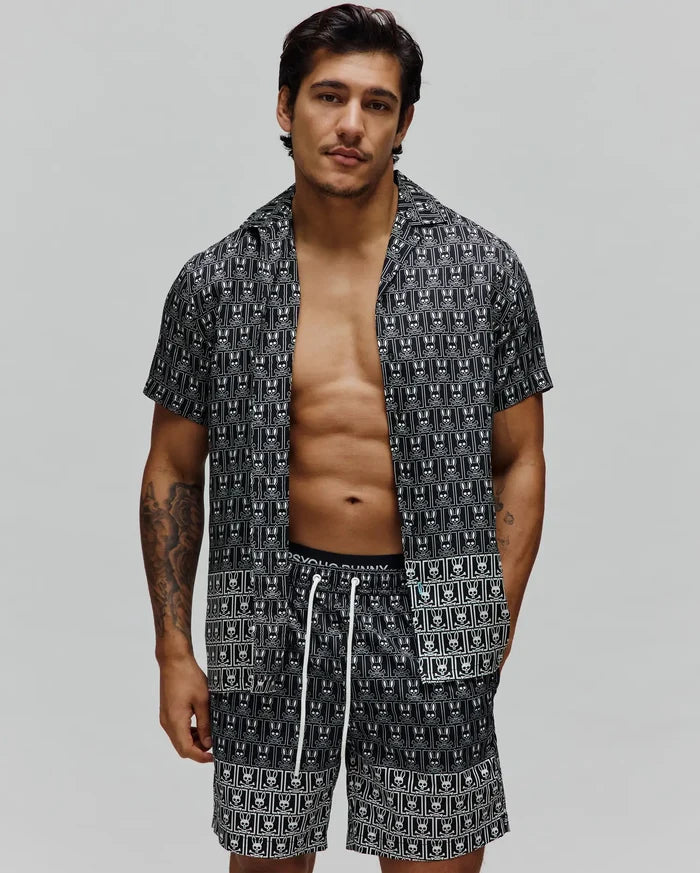 Mens Keon Tencel Shirt, a relaxed fit black short-sleeve button-up with an all-over white Psycho Bunny skull logo pattern, paired with matching shorts featuring white drawstrings.