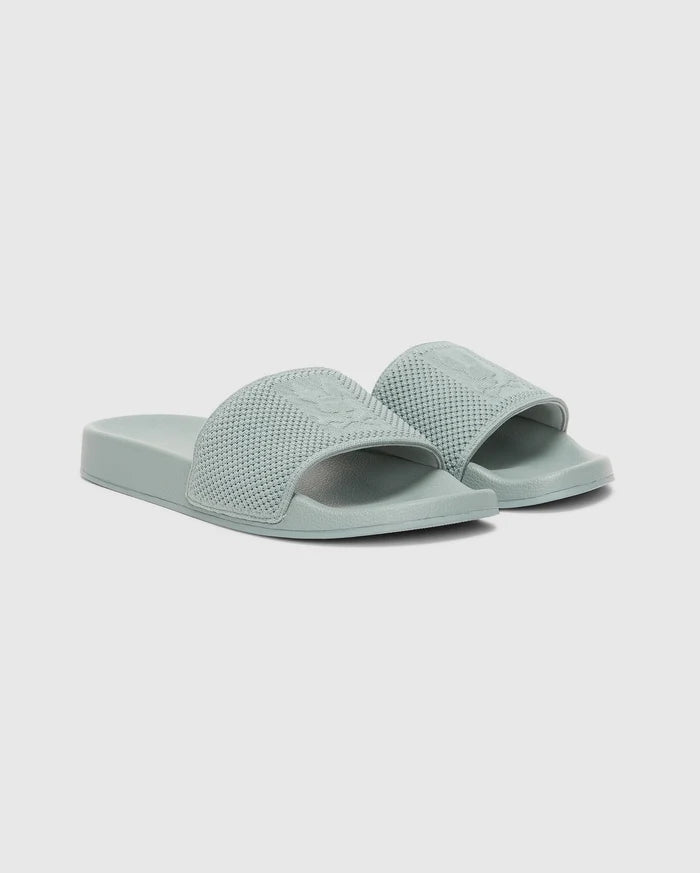 The Psycho Bunny MENS KNIT SLIDES - B6A474F200 are light green sandals with textured wide straps and an ergonomically molded footbed for comfort, shown on a plain white background.
