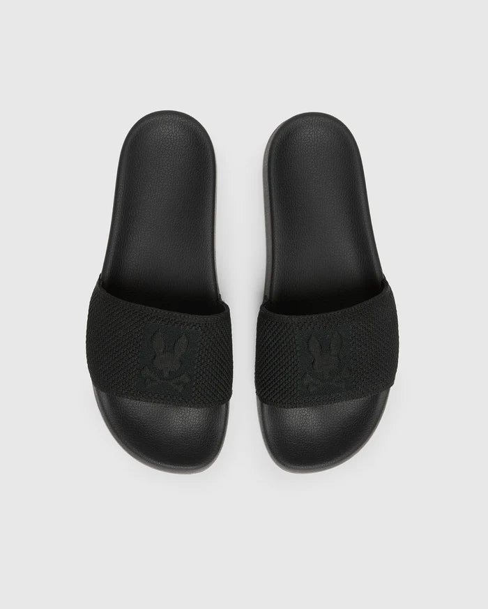 The Psycho Bunny MENS KNIT SLIDES - B6A474F200 are black slide sandals with textured straps and feature a flocked Bunny emblem design. They offer comfort with a molded footbed and are displayed on a plain light grey background.