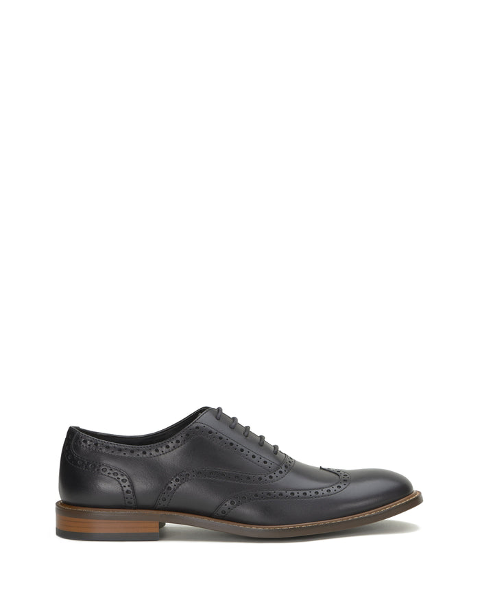 The Men’s Lazzarp Wingtip Brogue by Vince Camuto is shown in side profile on a white background, featuring black luxe leather with decorative perforations, a lace-up closure, and a brown sole. Crafted for all-day comfort with Flex365 technology.
