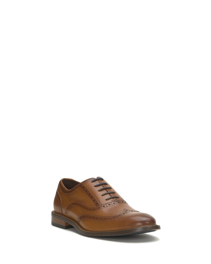 The Vince Camuto Men’s Lazzarp Wingtip Brogue is a single brown luxe leather dress shoe with decorative perforations in a classic wingtip design, featuring a low heel and thin laces, displayed on a white background—perfect for complementing any office outfit.