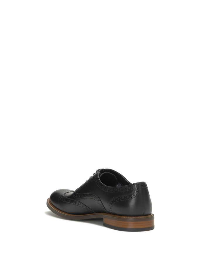 The Vince Camuto Men’s Lazzarp Wingtip Brogue is a luxurious black leather dress shoe with classic brogue detailing, pictured from the back left angle. This sophisticated wingtip features a brown sole and is photographed against a white background.
