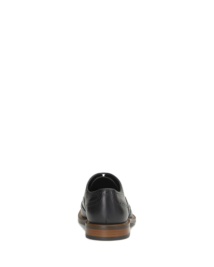 A single Vince Camuto Men’s Lazzarp Wingtip Brogue dress shoe in black luxe leather with brogue detailing, shown from the back to highlight the brown sole against a white background.