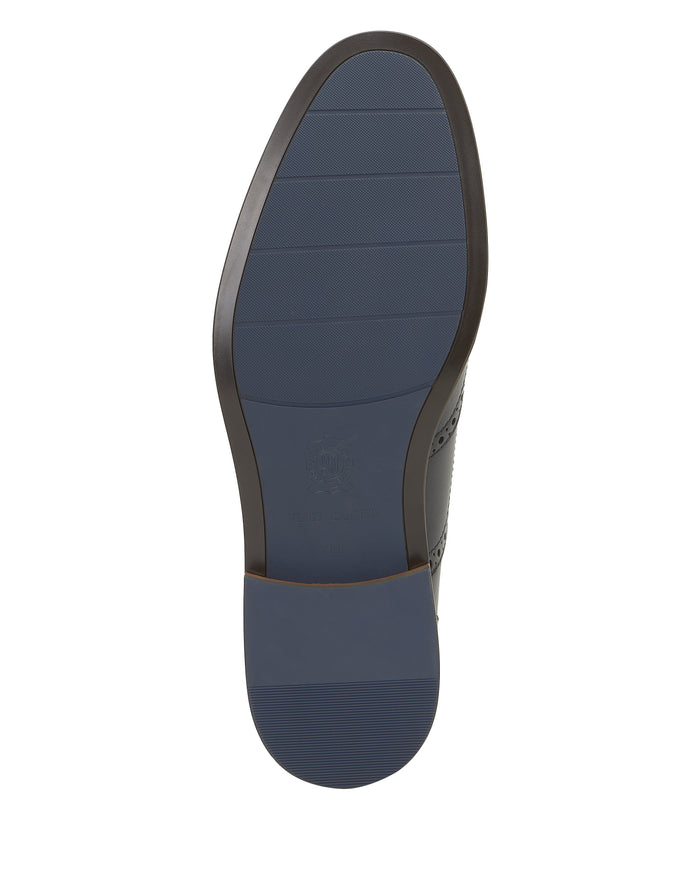 The image displays the distinctive blue rubber sole of the Vince Camuto Men’s Lazzarp Wingtip Brogue, highlighted by a subtly elevated heel and textured grip lines for enhanced traction. Designed to perfectly complement the luxe leather wingtip upper, this innovative sole features Flex365 technology for lasting comfort and flexibility with every stride.