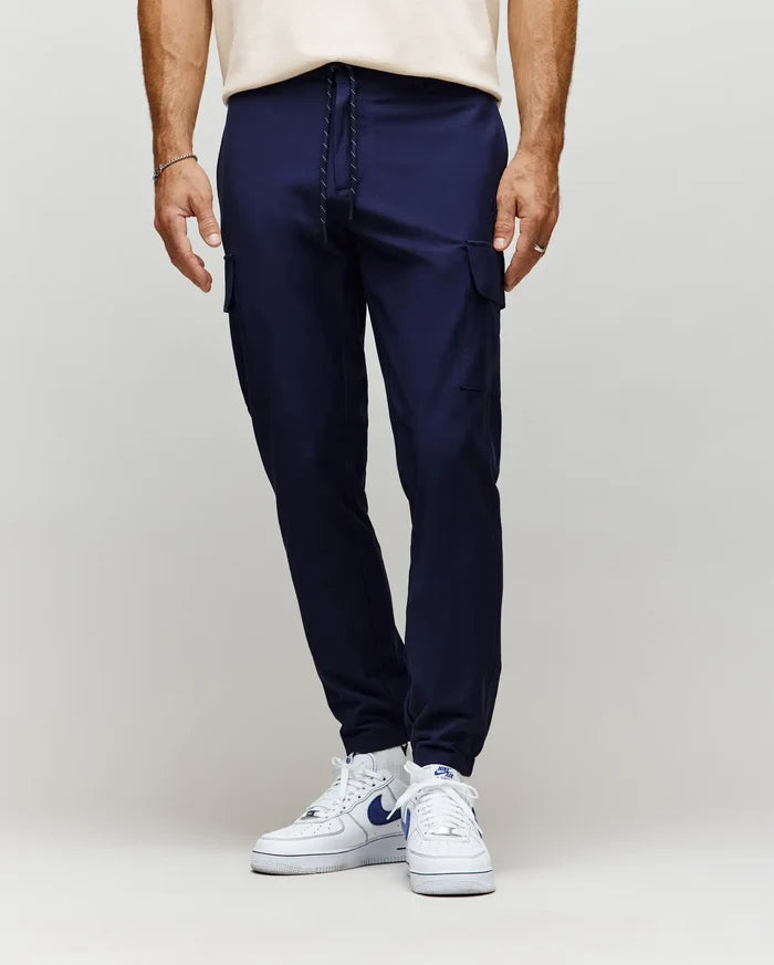Mens Lloyd Cargo Jogger in navy blue, featuring a slim, tapered fit, smooth fabric, side cargo pockets, and a black and white drawstring waist with ribbed cuffs.