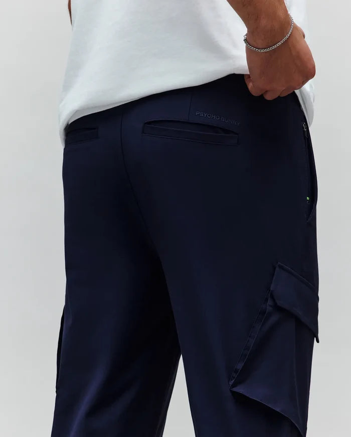 Mens Luka Cargo Pant in navy, featuring a relaxed fit, side cargo pockets, back welt pockets, and a tonal embroidered Psycho Bunny text logo on the back waistband with a subtle green zipper accent.