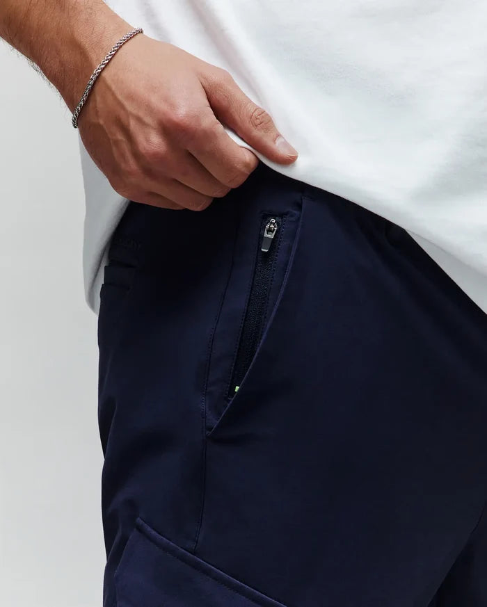 Mens Luka Cargo Pant in navy, featuring a zippered side pocket with a neon green accent, smooth woven fabric, and subtle embroidered Psycho Bunny branding on the waistband.