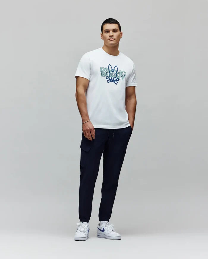 White classic fit jersey t-shirt with a large central gradient blue-green Psycho Bunny skull logo graphic, paired with navy Mens Luka Cargo Pant featuring side pockets and a drawstring waist.