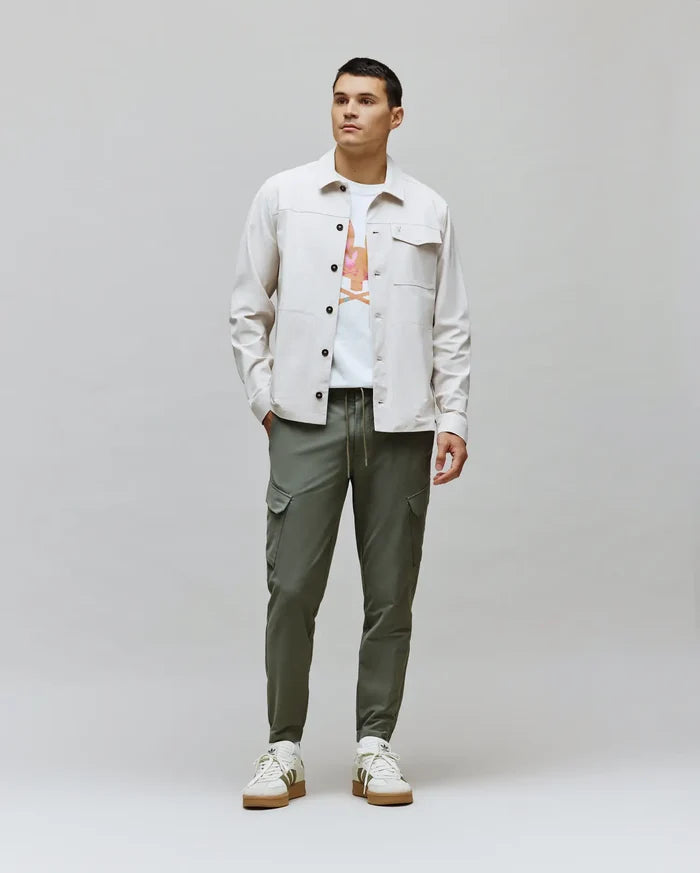 Mens Luka Cargo Pant in olive green, a white jersey t-shirt with a vibrant Psycho Bunny skull graphic, and a light beige classic fit overshirt with chest pockets.