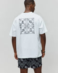 White Mens Luke Back Graphic Tee, relaxed jersey tee with a large black bandana graphic and four Psycho Bunny skull logos on the back, paired with black relaxed shorts with all-over white bandana-bunny skull pattern.