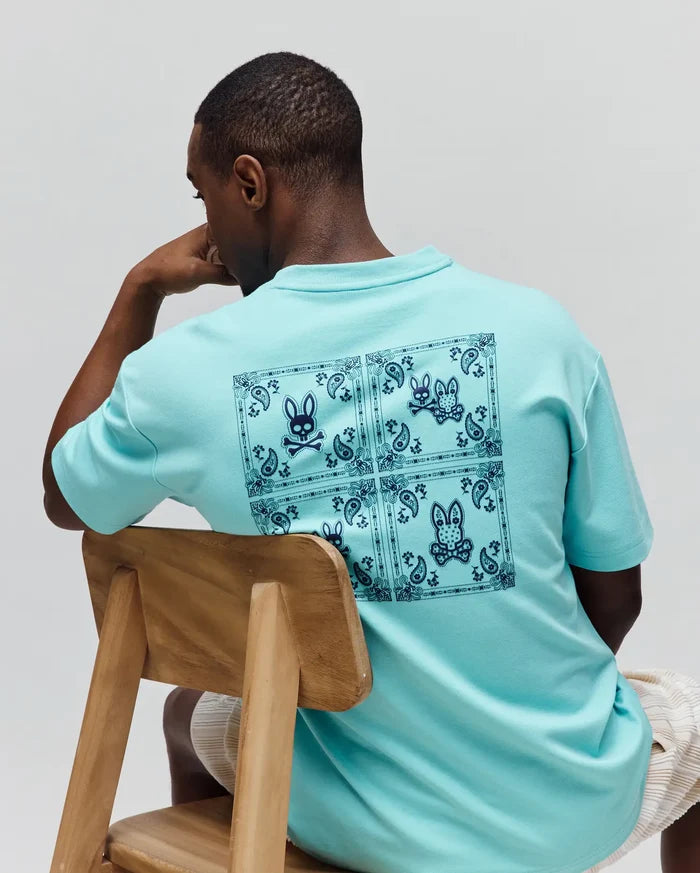 Mens Luke Back Graphic Tee in aqua, featuring a relaxed fit and smooth jersey knit. A large dark blue bandana-style graphic with multiple Psycho Bunny skull logos covers the entire back.