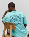 Mens Luke Back Graphic Tee in aqua, featuring a relaxed fit and smooth jersey knit. A large dark blue bandana-style graphic with multiple Psycho Bunny skull logos covers the entire back.