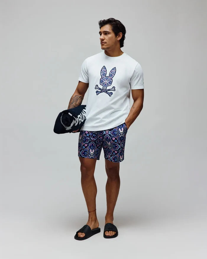 White classic fit jersey t-shirt with a large, colorful paisley Psycho Bunny skull logo on the chest, and Mens Luke Swim Trunk in navy with an all-over intricate pattern featuring small bunny skulls.