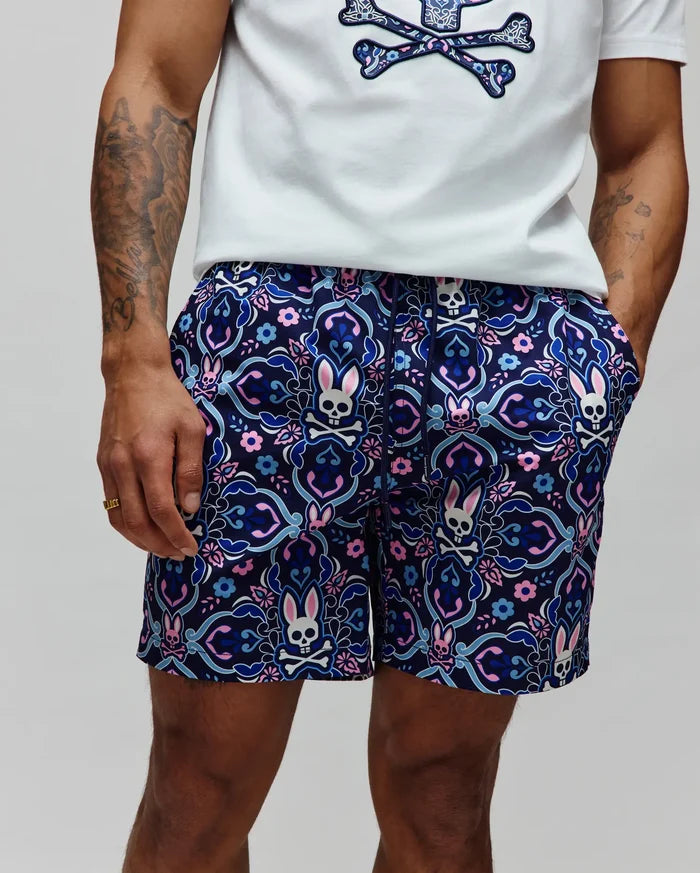 Mens Luke Swim Trunk in navy with an allover intricate floral and paisley pattern featuring repeated pink, light blue, and white Psycho Bunny skull logos, classic fit, smooth quick-dry fabric.