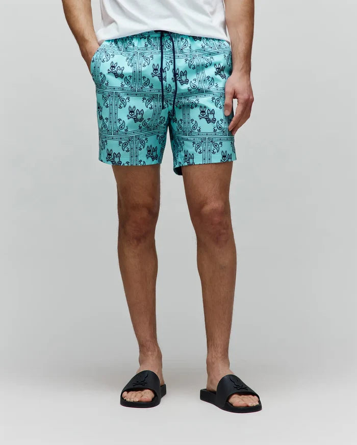 Mens Luke Swim Trunk, an aqua classic fit swim trunk with a dark blue all-over bandana print featuring the iconic Psycho Bunny skull logo and a drawstring waist, made from smooth quick-dry fabric.