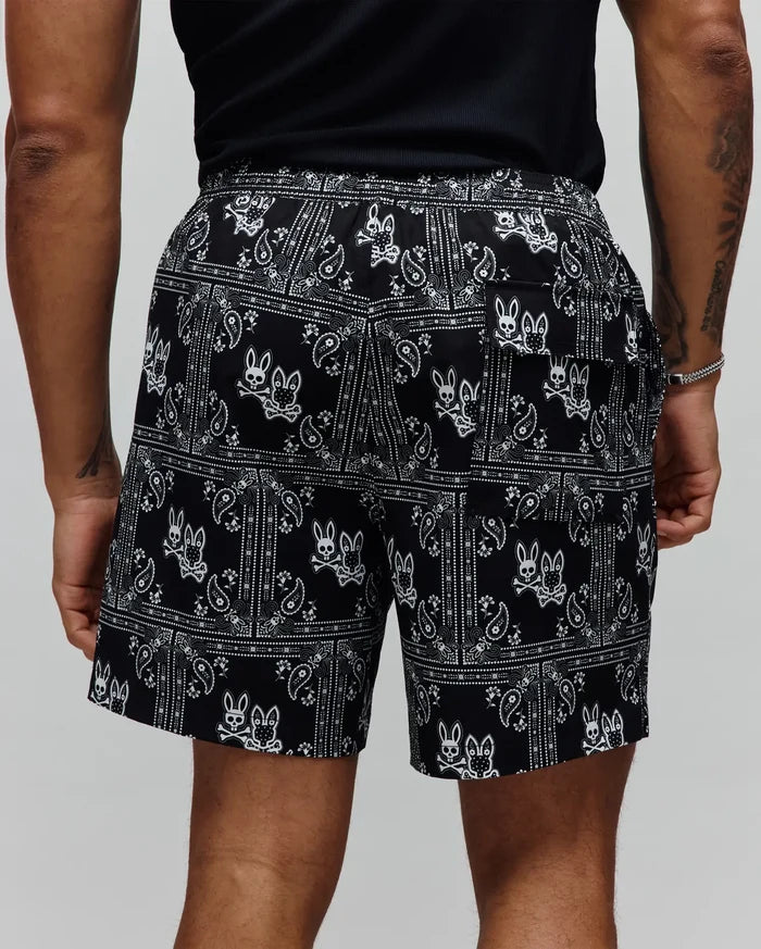 Mens Luke Swim Trunk in black with a white all-over bandana paisley print and repeated Psycho Bunny skull logos, featuring a relaxed fit and smooth fabric.