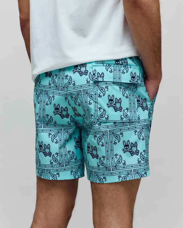 Mens Luke Swim Trunk in aqua with a navy blue all-over bandana paisley print featuring the iconic Psycho Bunny skull logo, relaxed fit, smooth quick-dry fabric, with side and back flap pockets.