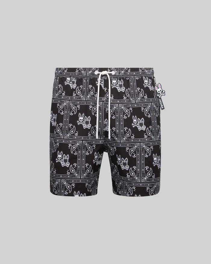 Mens Luke Swim Trunk, black with white all-over bandana print featuring the iconic Psycho Bunny skull logo, relaxed fit, smooth quick-dry fabric, white drawstring, and small Psycho Bunny tag.
