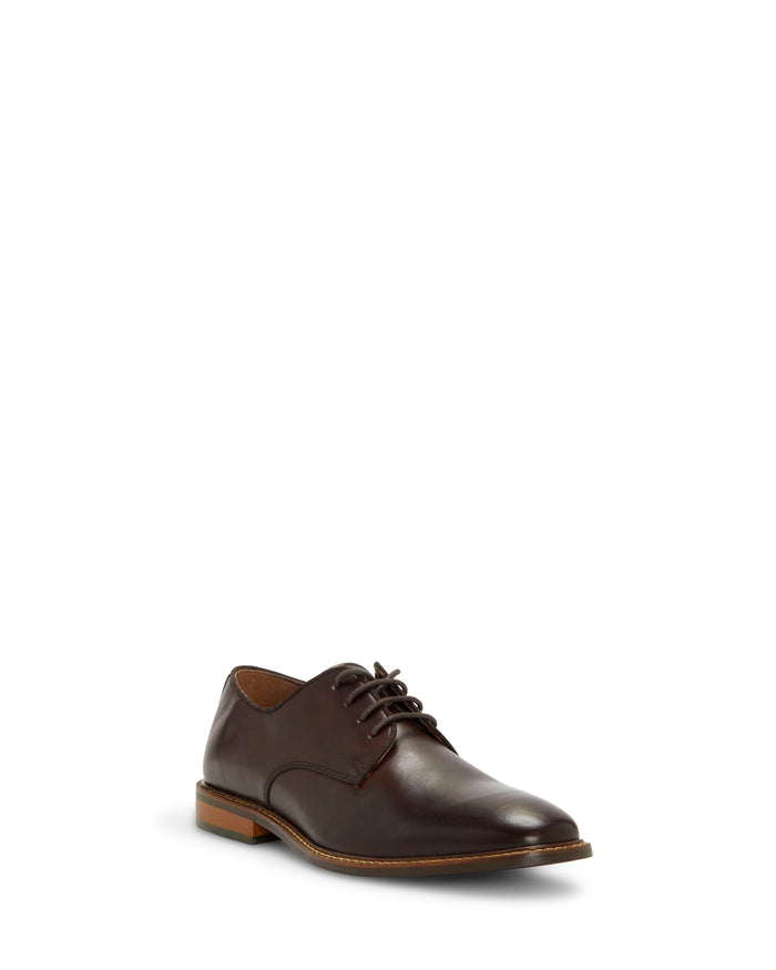 The Vince Camuto Men’s Lyre Derby, a single dark brown leather dress shoe with laces, a low heel, and a tan sole, exudes timeless style and is displayed on a plain white background.