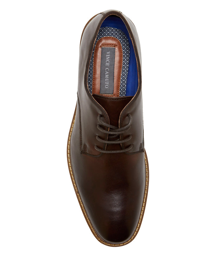A top-down view of the Vince Camuto Men’s Lyre Derby showcases a brown leather dress shoe with classic laces. The inner sole is finished with a blue trim and displays the VINCE CAMUTO label, while the dark leather upper contrasts with a light brown outer sole for an elegant, timeless appeal.