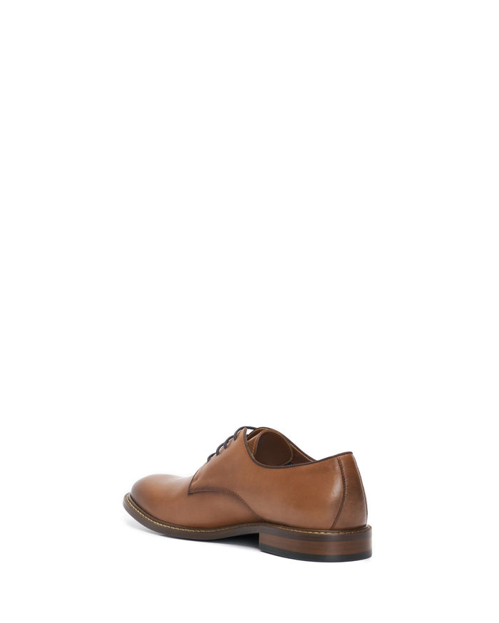 A single Men’s Lyre Derby dress shoe by Vince Camuto is displayed from a rear angle against a white background. Constructed from dark brown leather, this classic shoe features laces and a dark sole with visible edge stitching, embodying timeless style.