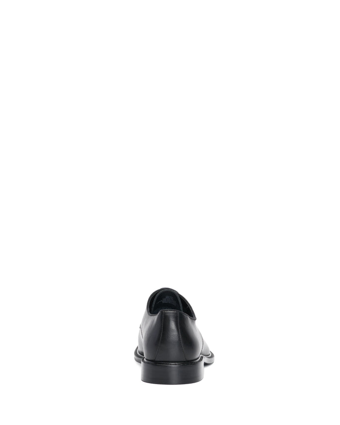 A single Vince Camuto Men’s Lyre Derby black dress shoe, crafted from dark leather and shown from the back, is centered against a plain white background to showcase its classic style.