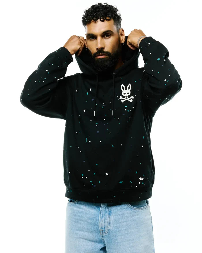 Mens Malcom Splatter Hoodie, a black relaxed fit soft jersey hoodie featuring a vibrant white and teal splatter print and a large white Psycho Bunny skull logo on the left chest.