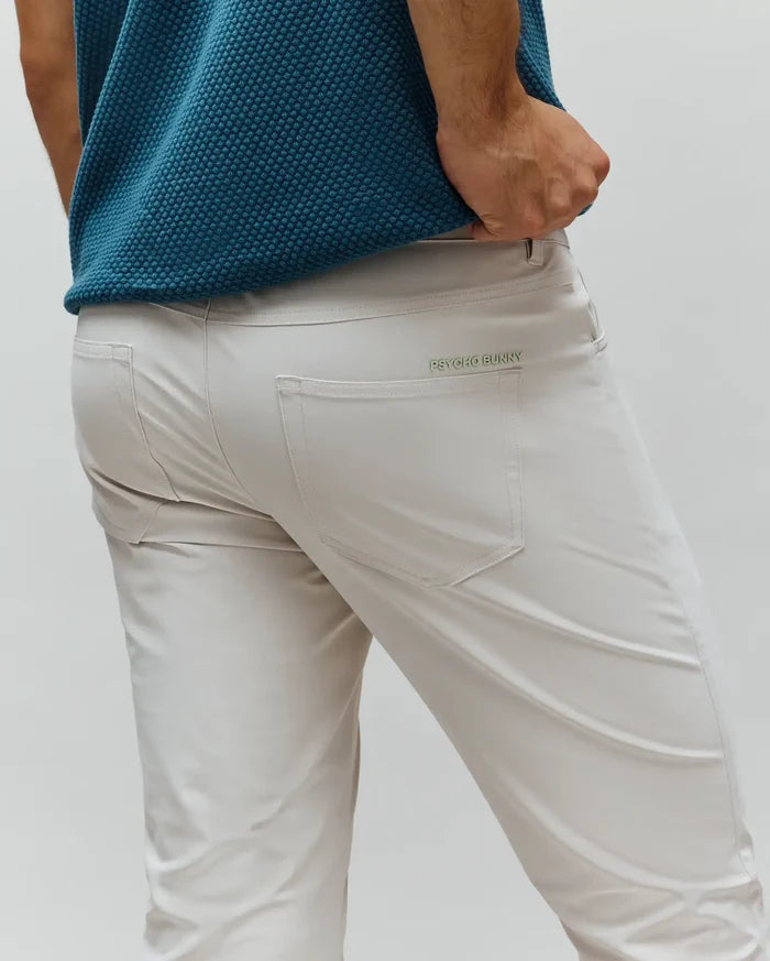 Mens Maverick 10k Step Pant, light beige slim-fit performance fabric with a small, embroidered green Psycho Bunny wordmark above the back right pocket.