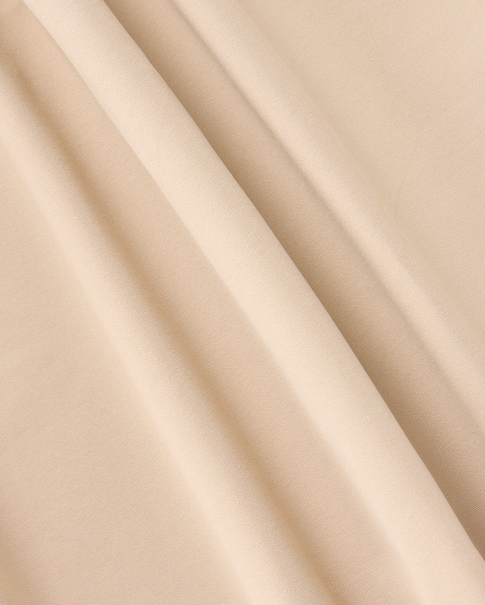 A close-up of beige fabric with a smooth texture and gentle folds creating soft shadows. The material appears lightweight with a plain weave, ideal for crafting the versatile MENS 10K STEP PANT - B6P788D200 by Psycho Bunny, featuring its stylish five-pocket design.