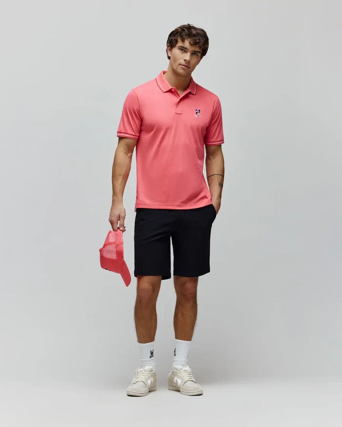 Coral pink pique polo with white tipped collar and cuffs, featuring a small embroidered blue and red Psycho Bunny skull logo on the left chest, paired with classic fit black Mens Maverick 10k Step Short.