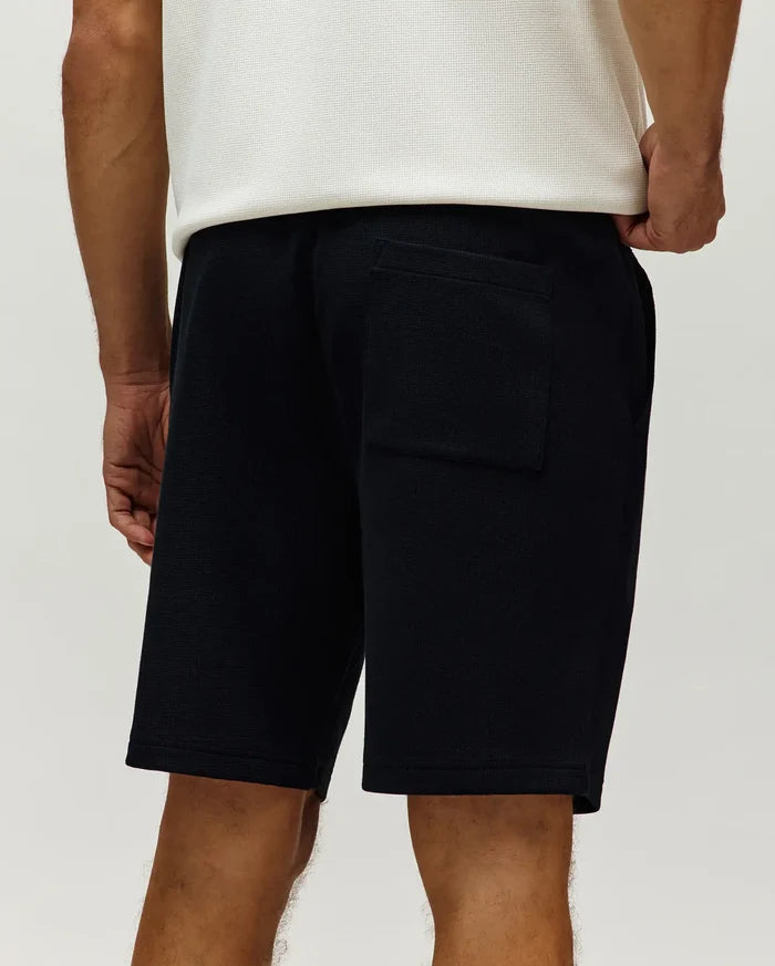 Black Mens Maxton Waffle Sweatshort, a relaxed fit streetwear style, featuring a textured waffle knit fabric, side pockets, and a back patch pocket.