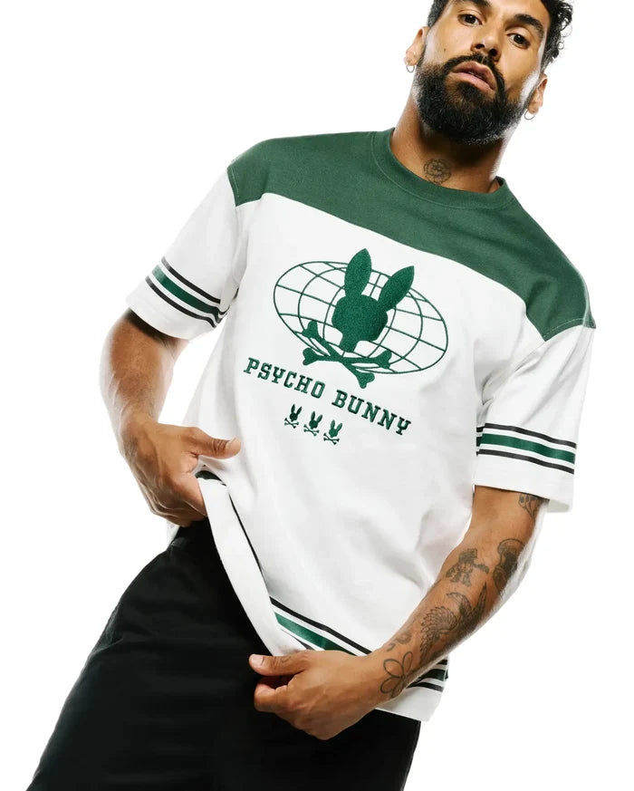 Mens Mike Graphic Jersey Tee, a relaxed fit white jersey tee with green color block shoulders, black and green striped sleeves, and a large central embroidered green Psycho Bunny skull globe graphic with text and three small skull logos.