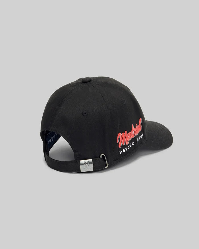 The Psycho Bunny MENS MONTREAL BASEBALL CAP (MO1500048) is a black 100% cotton cap with "Montreal PSYCHO PRINT" embroidered in red and white on the back left, plus an adjustable strap and metal buckle, shown on a light gray background.