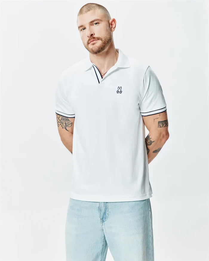 Mens Nasser Polo, white pique knit, classic fit, with navy blue striped collar and cuffs, featuring a small embroidered Psycho Bunny skull logo on the left chest.