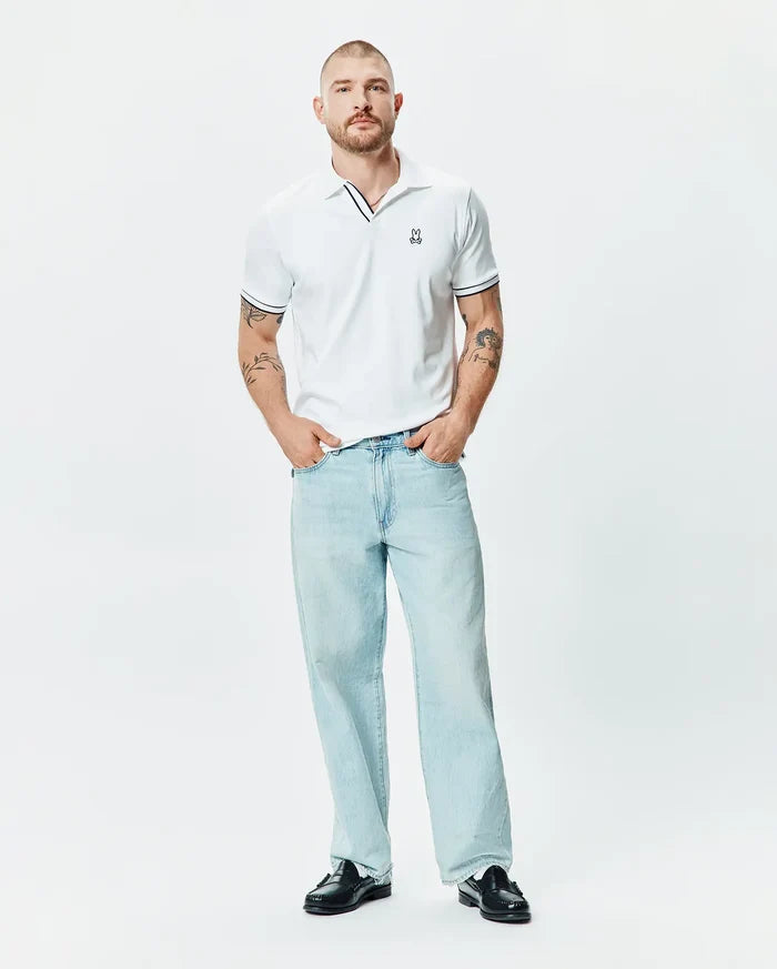 Mens Nasser Polo, a classic fit white pique polo with black tipping on the collar and sleeve cuffs, featuring a small embroidered Psycho Bunny skull logo on the left chest.