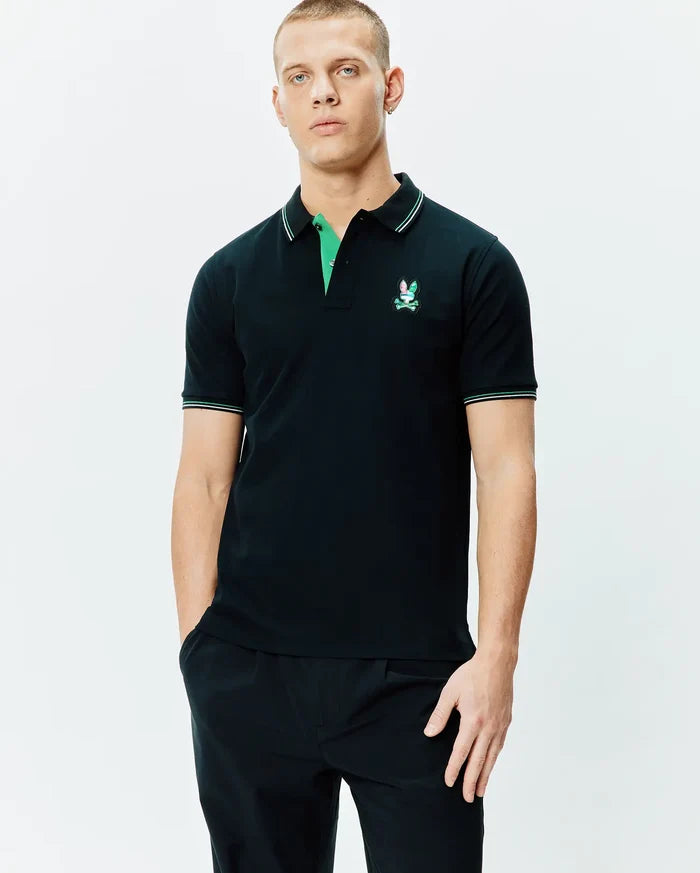 Mens Nate Pique Polo, a classic fit black pique polo with a vibrant green undercollar, white and green striped collar and cuffs, featuring an embroidered multi-color Psycho Bunny skull logo on the left chest.