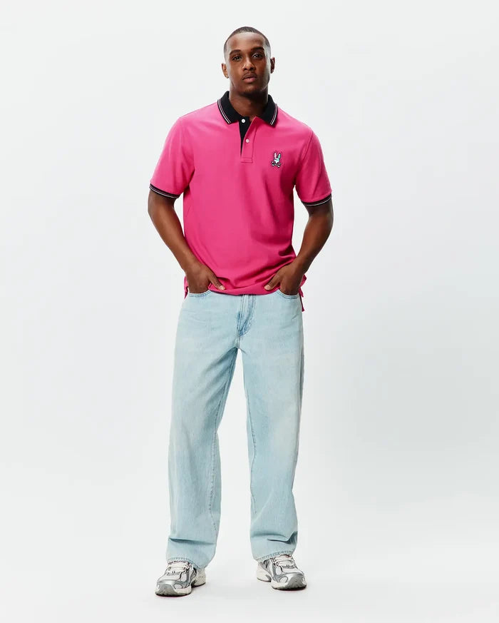 Mens Nate Pique Polo in vibrant pink, featuring a classic fit, black ribbed collar and cuffs with white tipping, and a small embroidered Psycho Bunny skull logo on the left chest.