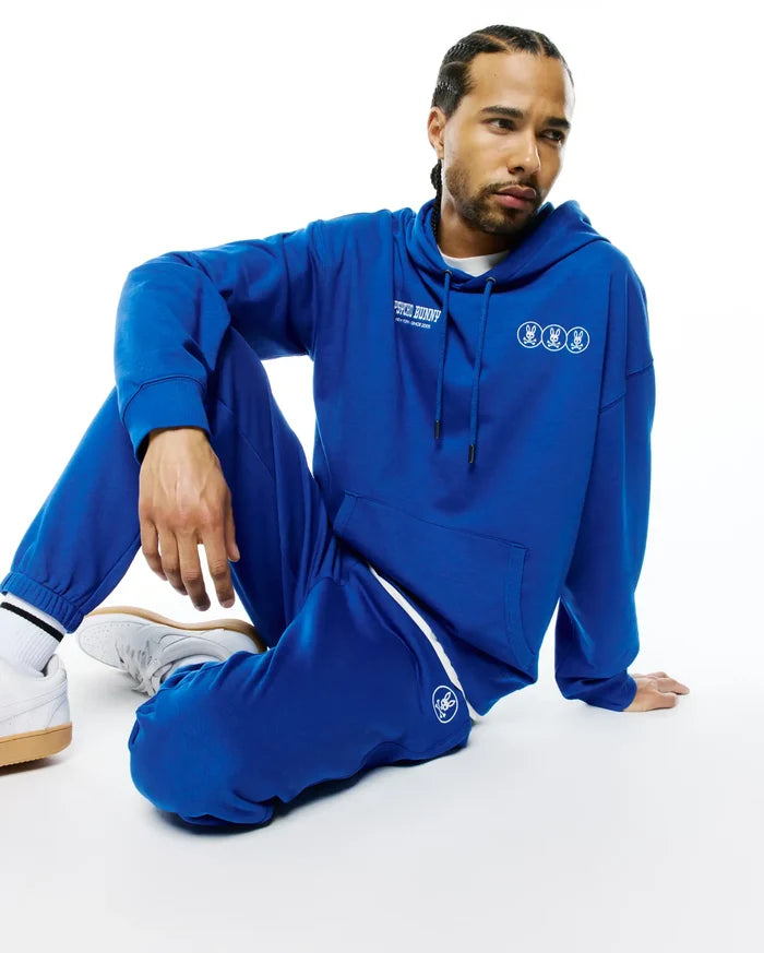 Royal blue relaxed fit French terry hoodie with white Psycho Bunny text and triple bunny skull chest logos, paired with matching Mens Nathaniel Sweatpant featuring a white side stripe and left thigh bunny skull logo.