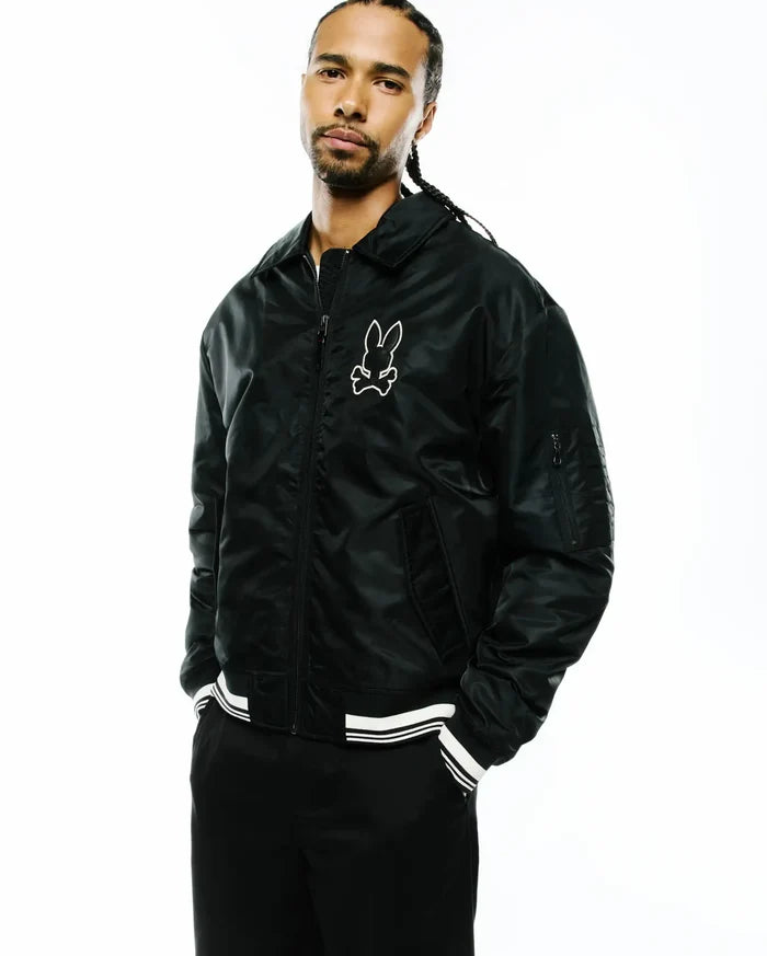 Mens Nathaniel Satin Coach Jacket, black with a relaxed fit, featuring a shiny satin texture, full zip, classic collar, white striped ribbed cuffs and hem, and a large white embroidered Psycho Bunny skull logo on the left chest.