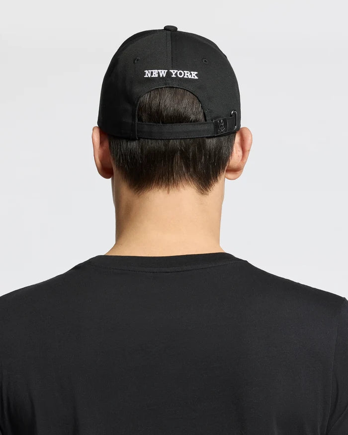 A person shown from behind against a plain background wears a woven black cotton T-shirt and the Psycho Bunny MENS NEW YORK BASEBALL CAP - MO1500012, featuring "NEW YORK" embroidered on the back.