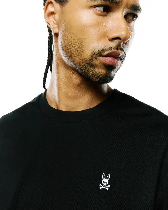 Mens Norman Long Sleeve Oversized Fit Tee in black premium jersey knit, featuring a small, white embroidered iconic Psycho Bunny skull logo prominently on the left chest.