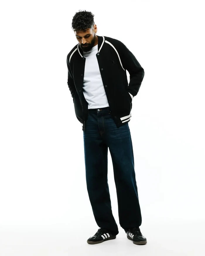 Black knit Mens Rafferty Cardigan, a classic fit varsity style featuring white shoulder piping, ribbed cuffs with double white stripes, and a small embroidered Psycho Bunny skull logo on the left chest.