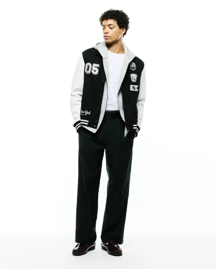 Mens Reilly Knit Coach Jacket: Black and white varsity style jacket with a layered grey hood, featuring a large 05 patch, embroidered Psycho Bunny skull, and New York script.