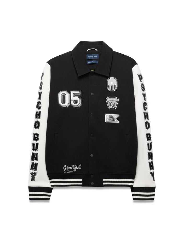 Mens Reilly Knit Coach Jacket, black with white sleeves, features embroidered 05, New York text, multiple Psycho Bunny skull logo patches, and vertical PSYCHO BUNNY text on sleeves, with striped cuffs and hem.