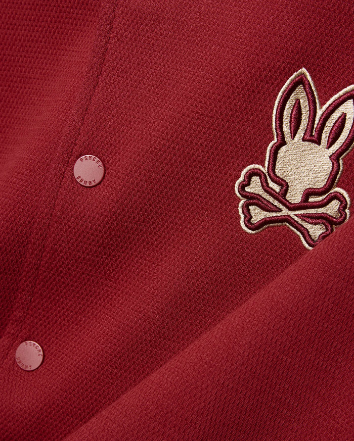 Mens Reilly Knit Bomber in deep red pique knit, featuring a large embroidered gold and burgundy Psycho Bunny skull logo on the chest and matching branded buttons.