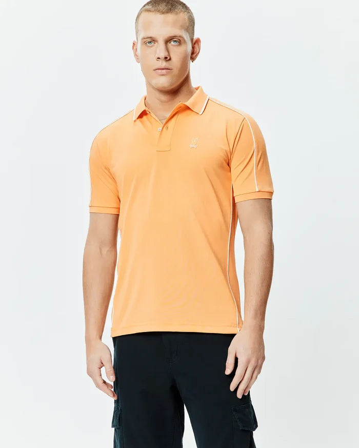 Mens Rhys Sport Polo, vibrant orange smooth performance jersey with white piping on shoulders and sides, classic fit, and small embroidered Psycho Bunny skull logo on left chest.